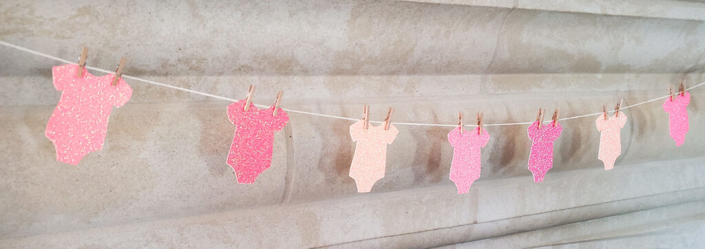 Handmade bottle and onesie garlands crafted from pink glitter cardstock, hanging as festive party décor.