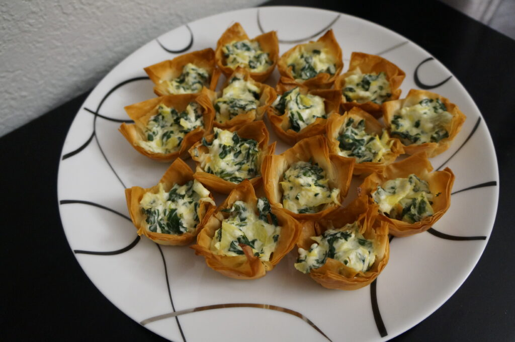 Finished phyllo shells filled with creamy dip, ready to serve as bite-sized appetizers.