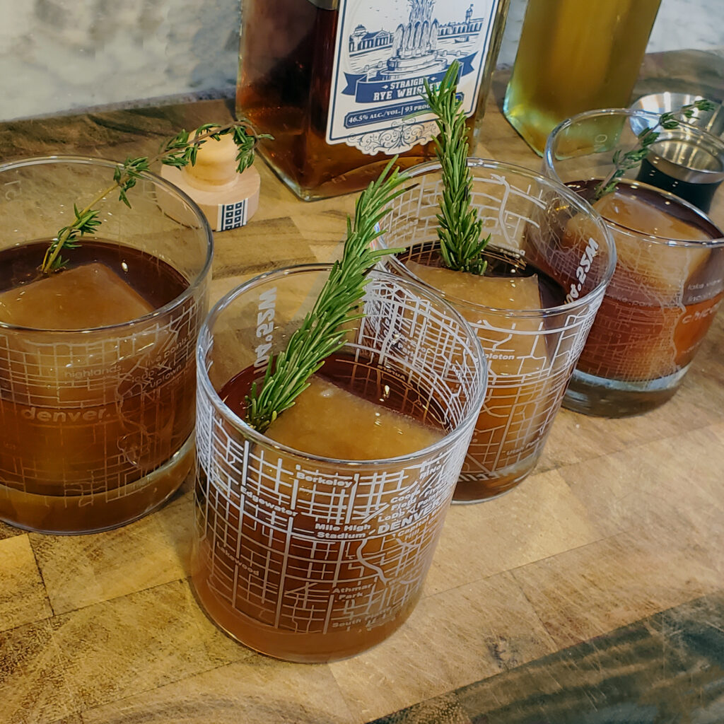 Old Fashioned cocktail garnished with orange peel and apple cider ice cube, served in a rocks glass.