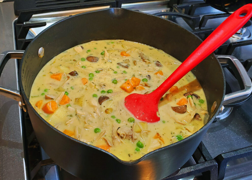 Pot pie filling with turkey, vegetables, and herbs simmering in a stockpot.