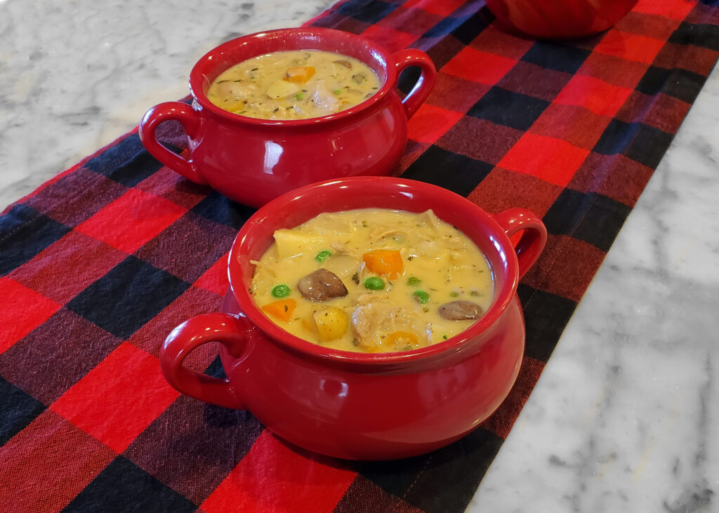 Oven-safe bowls filled with turkey pot pie filling and ready to be topped with raw pie crust.