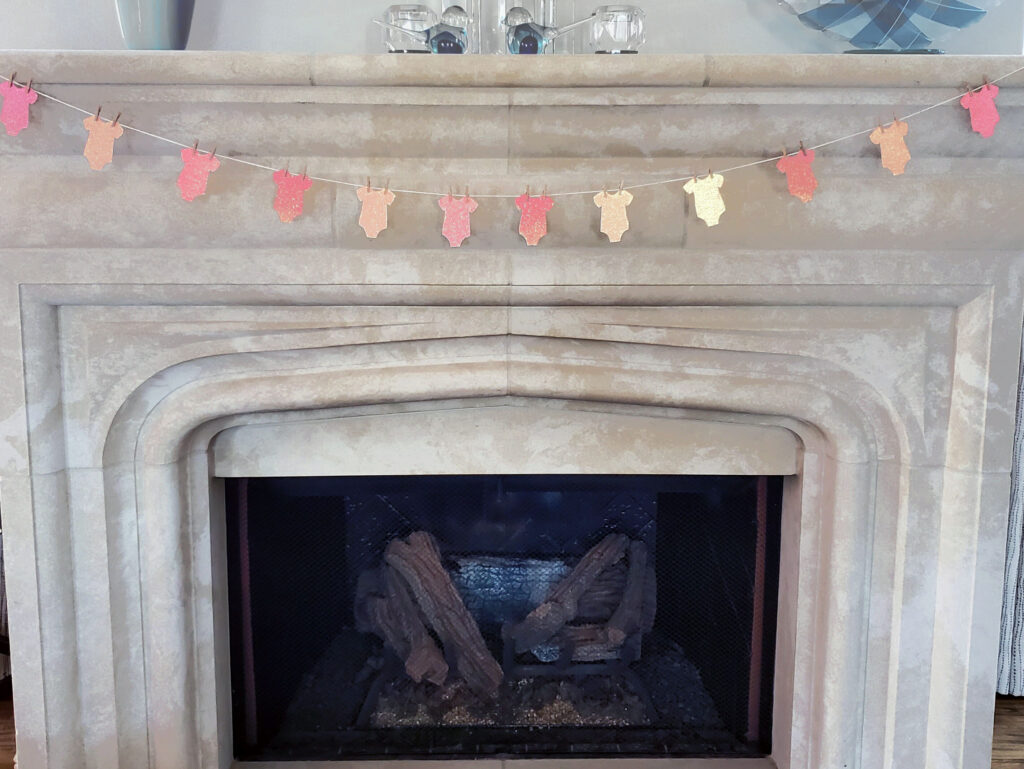 Handmade onesie garland crafted from pink glitter cardstock, hanging as festive party décor.
