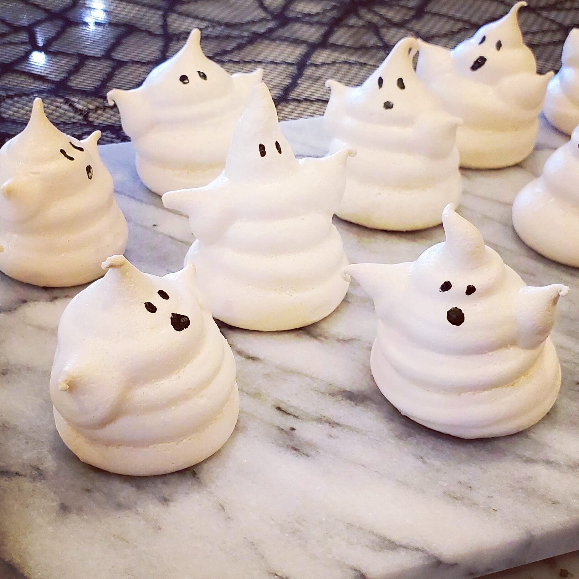 White ghost-shaped meringue cookies with candy eyes, fully dried and crisp, arranged on plate.