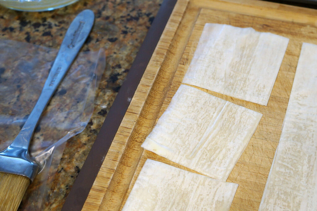 Phyllo sheets layered and brushed with melted butter on a cutting board during assembly.