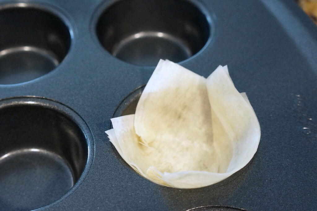 Layered phyllo dough pressed into a mini muffin pan before baking to form crisp appetizer cups.