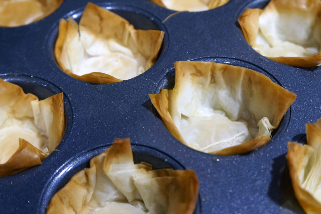 Golden-brown phyllo shells cooling after baking, showing crisp edges and cup shape.
