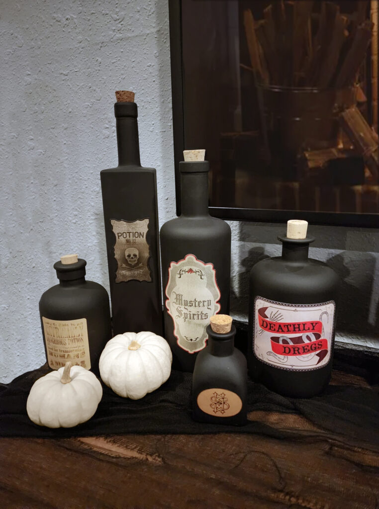 DIY black potion bottles made from recycled liquor bottles with vintage-style labels for Halloween decor.
