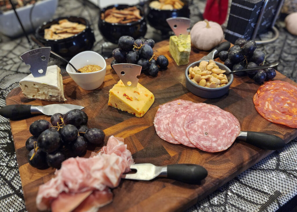 Halloween charcuterie board with dark cheeses, smoked meats, grapes, and olives.
