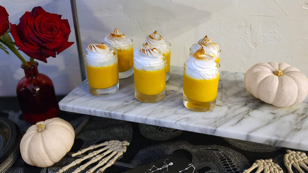 Pumpkin pie shooters layered in clear shot glasses with creamy pumpkin filling and whipped topping.
