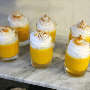 Pumpkin pie shooters layered in clear shot glasses with creamy pumpkin filling and whipped topping.