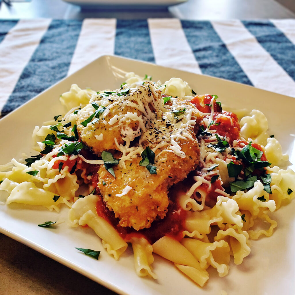 Golden chicken parmesan served over pasta with tomato sauce and grated Parmesan.