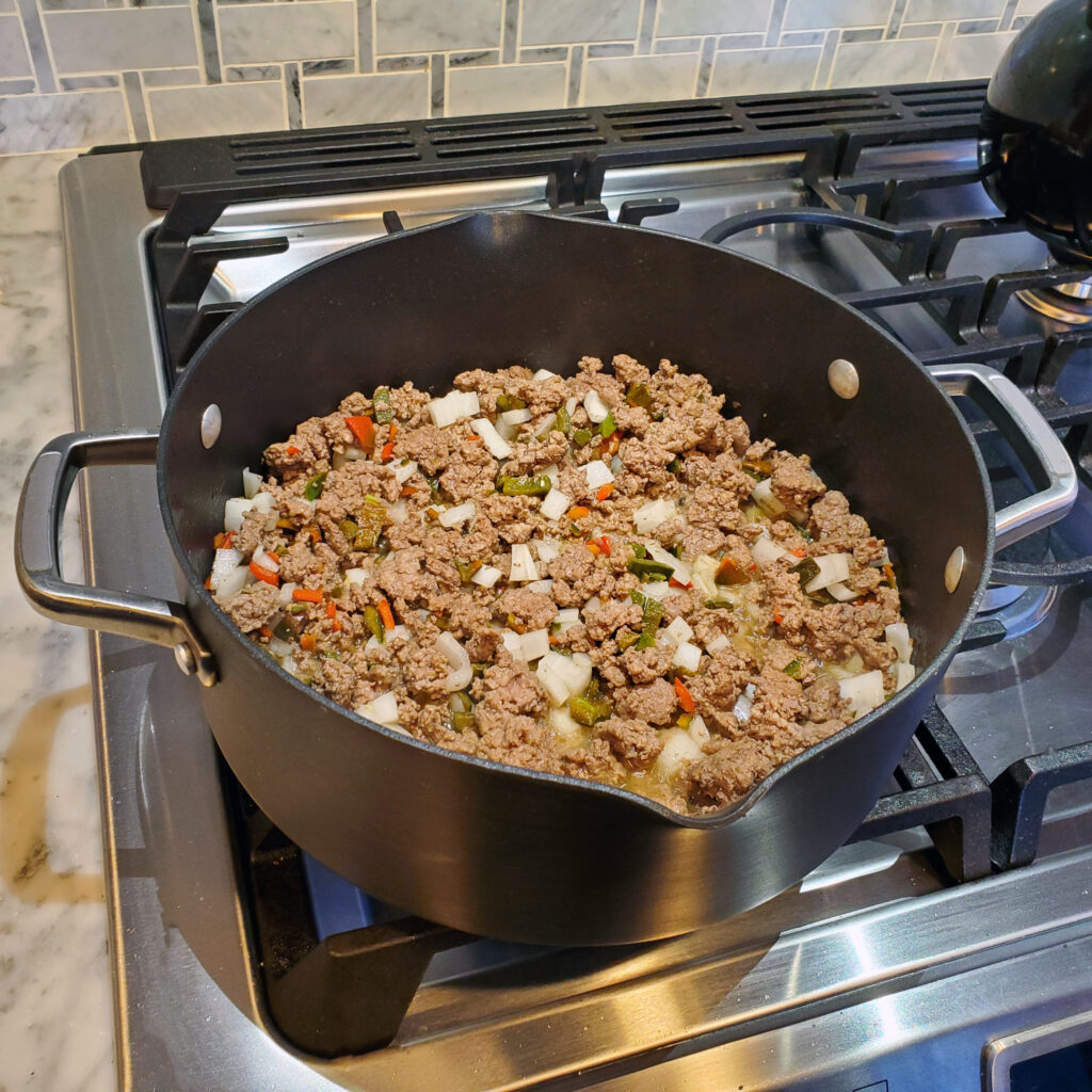 Chili cooking in a pot with beef, pork, and smoky spices during the simmering stage.