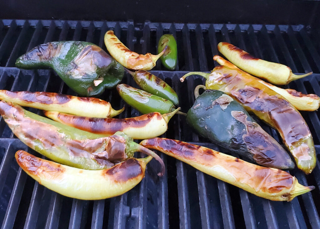Assorted chiles and red onion grilling over high heat, developing char and smoky flavor for roasted salsa verde.