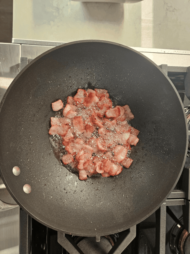 Brussels sprouts cooking in a wok with rendered bacon fat, showing light charring and golden edges