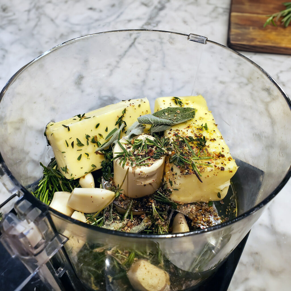 Fresh herbs and butter being blended in a food processor to make compound butter.