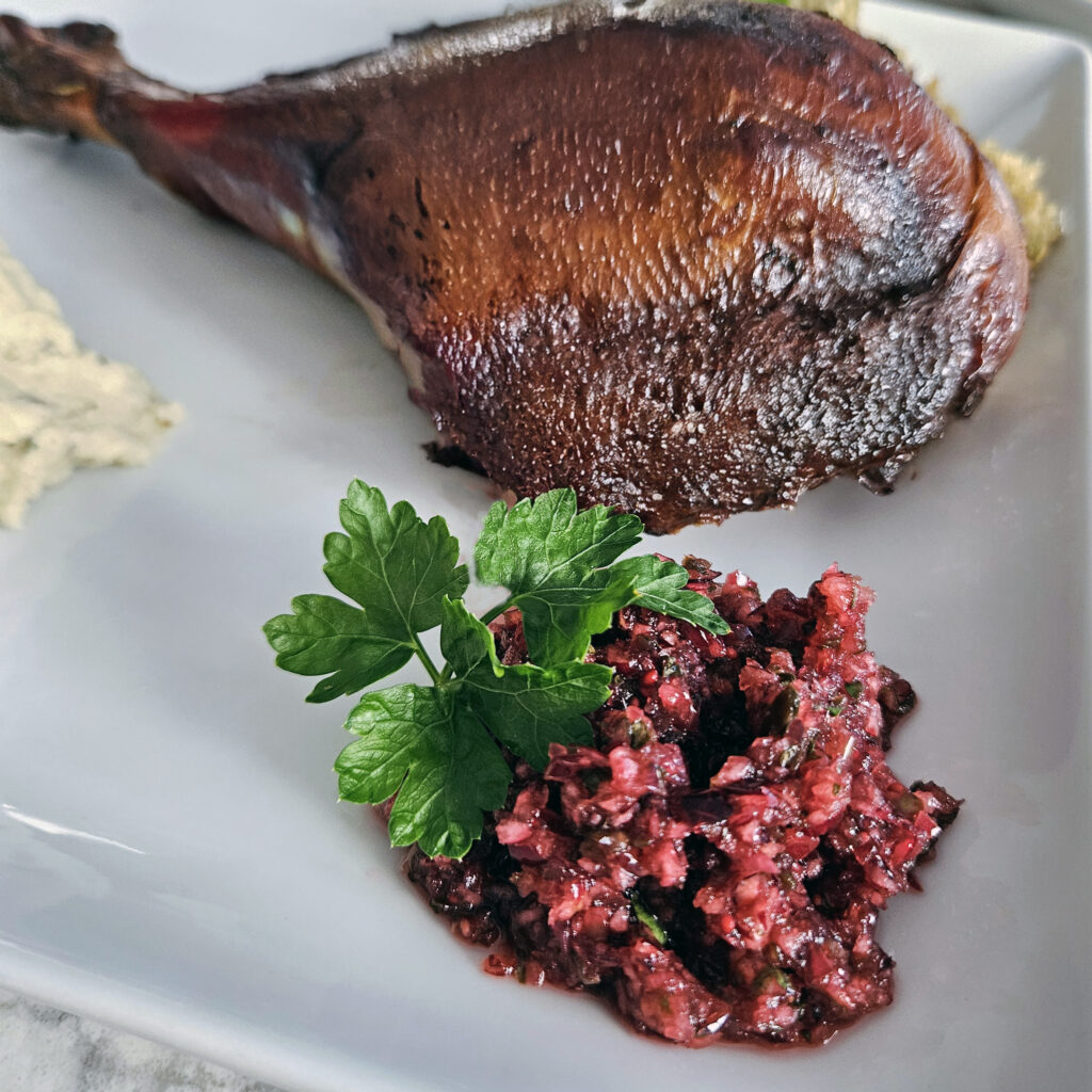 Cranberry salsa served alongside a roasted turkey leg on a Thanksgiving plate, highlighting the bright red salsa as a fresh, colorful contrast to the golden-brown turkey.