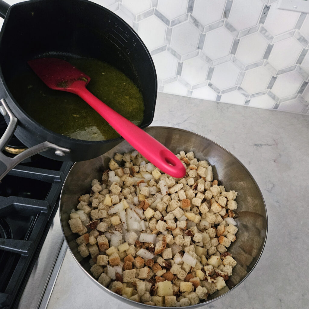 Dry stuffing ingredients being tossed with melted herb butter and turkey broth.