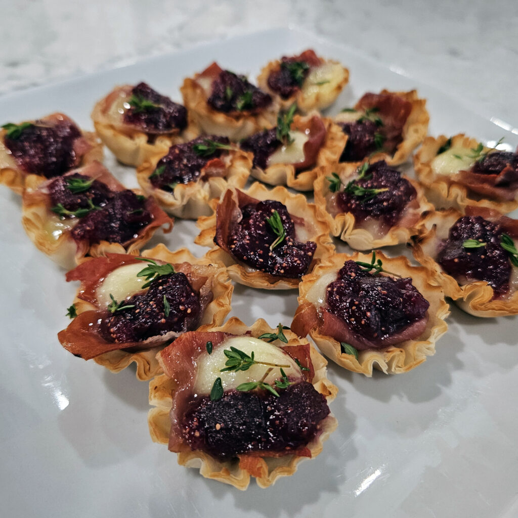 Fig jam served in a phyllo cup with melted brie and fresh thyme garnish.