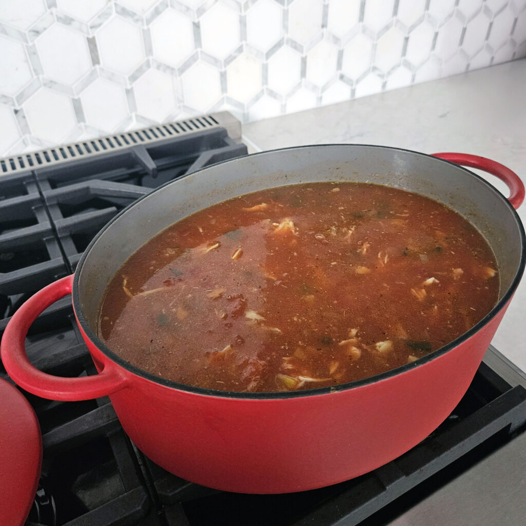 Soup simmering in a Dutch oven with visible chicken and vegetables.
