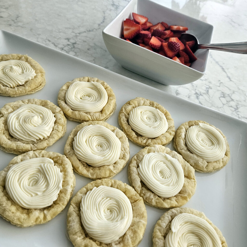 Sweetened cream cheese being spooned into pastry centers before baking.