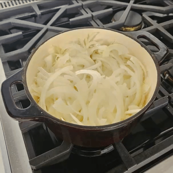 Thinly sliced onions slowly browning in a pot on the stovetop.