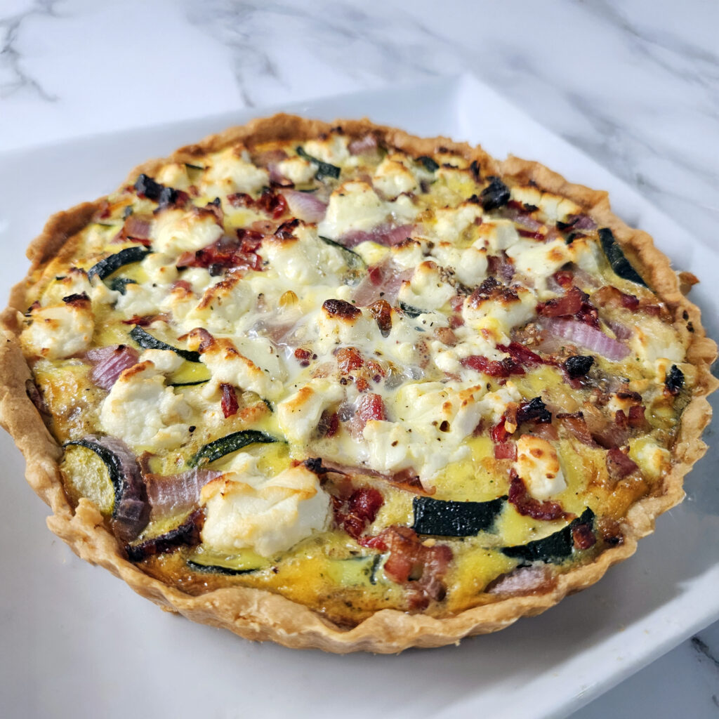 Golden farm quiche with goat cheese and vegetables sliced and served on a plate.