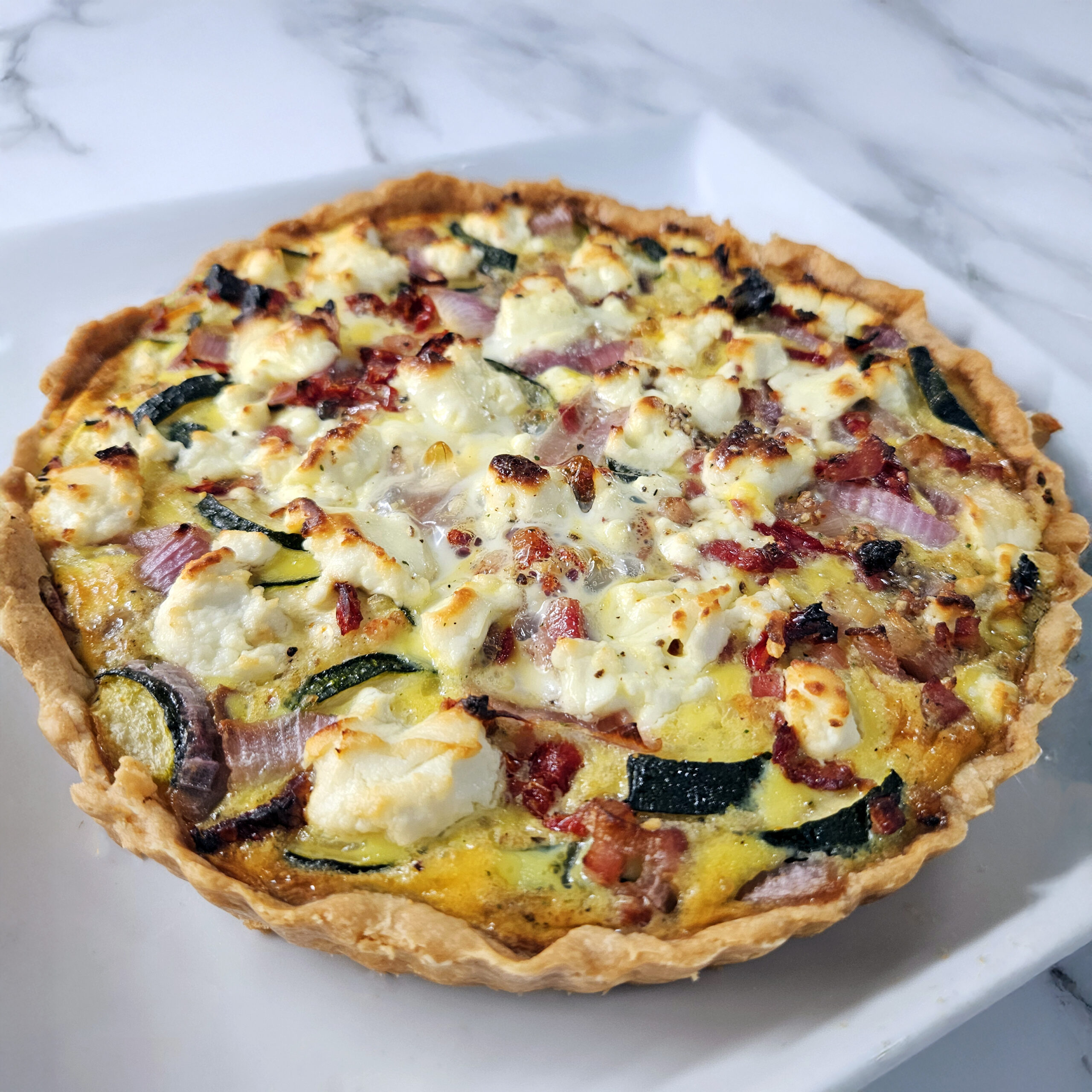 Golden farm quiche with goat cheese and vegetables sliced and served on a plate.