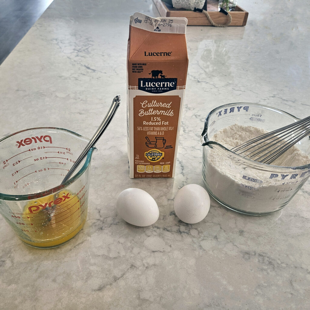 Chicken thighs being dredged in seasoned flour beside a bowl of buttermilk marinade, showing the breading process before frying.