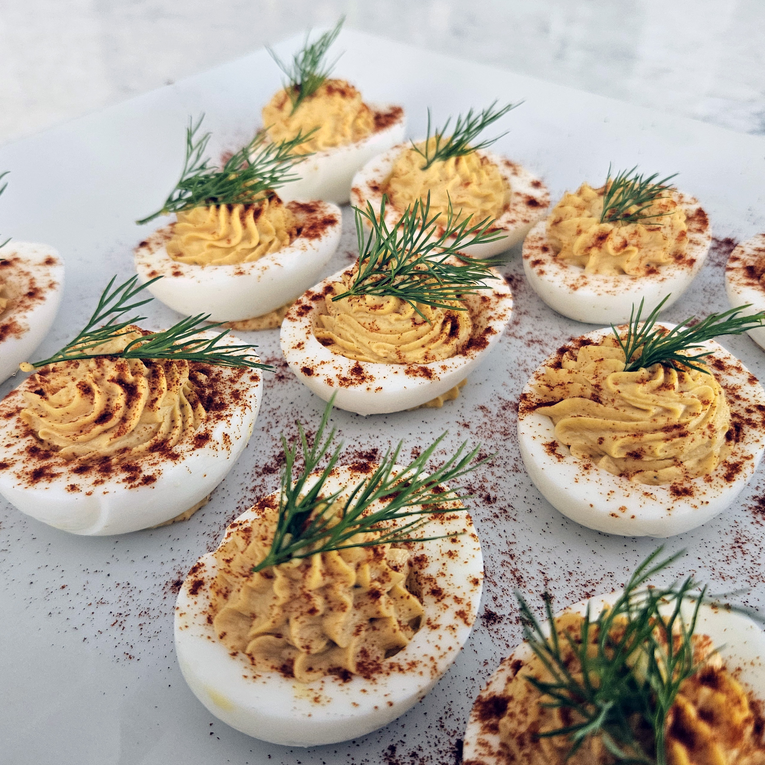 Deviled eggs topped with dill sprigs and seasoned filling, arranged on a serving platter.