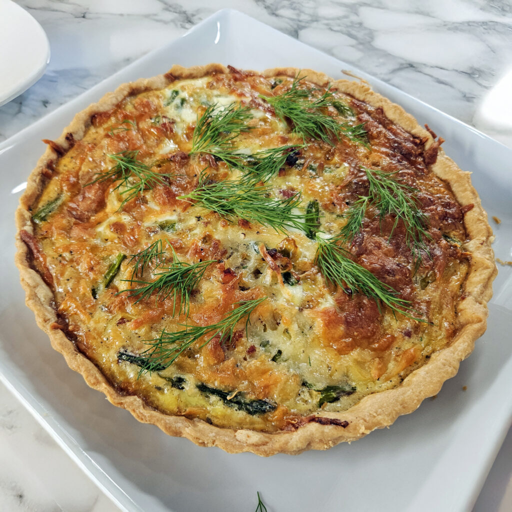 Baked quiche in a tart pan showing flaky crust and vegetable filling.