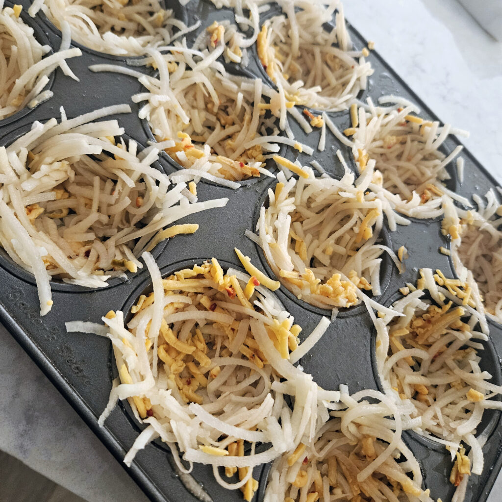 Crispy hash brown nests pressed into a muffin tin before adding egg filling.