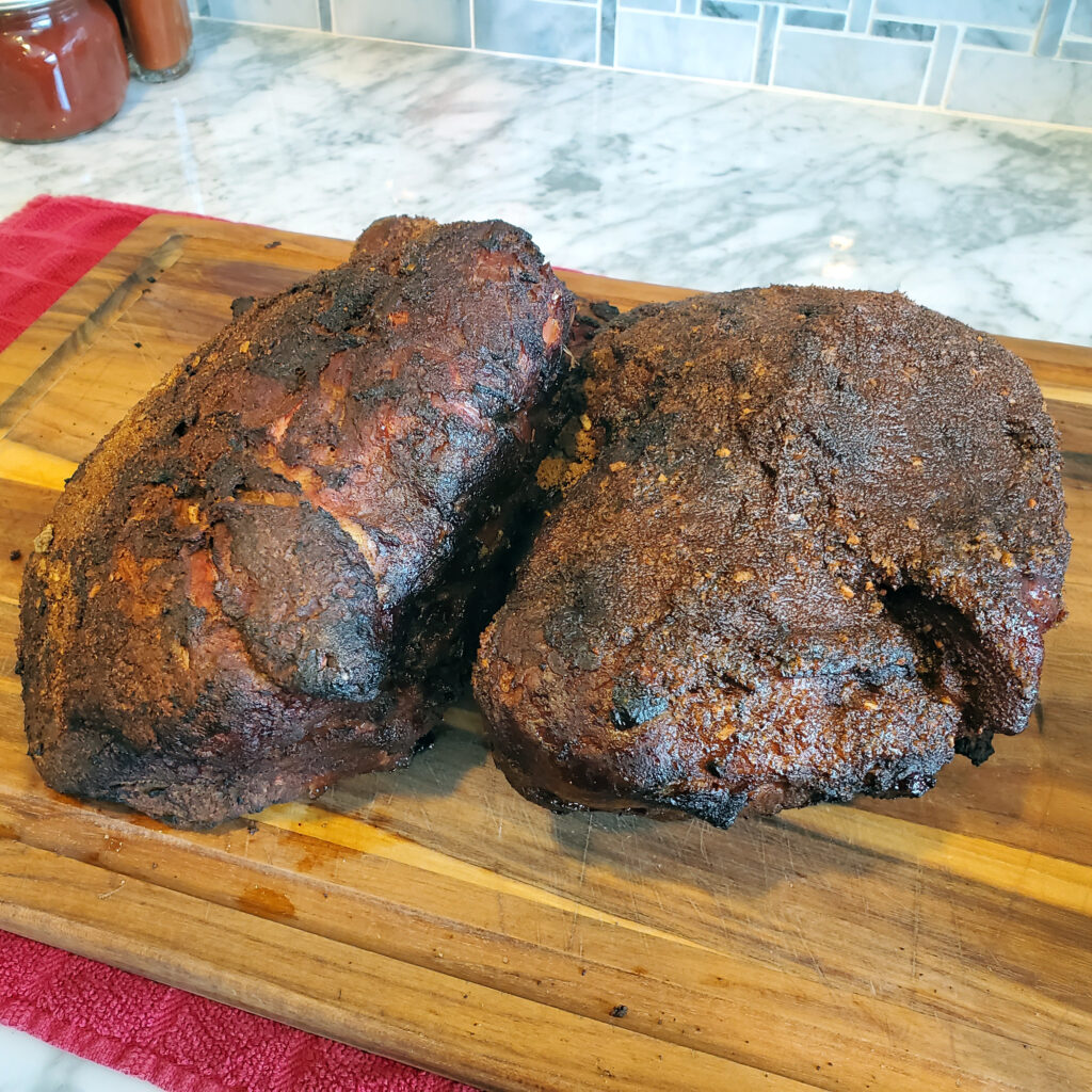 Tender pulled pork with visible bark and smoke ring, ready to be shredded and served.