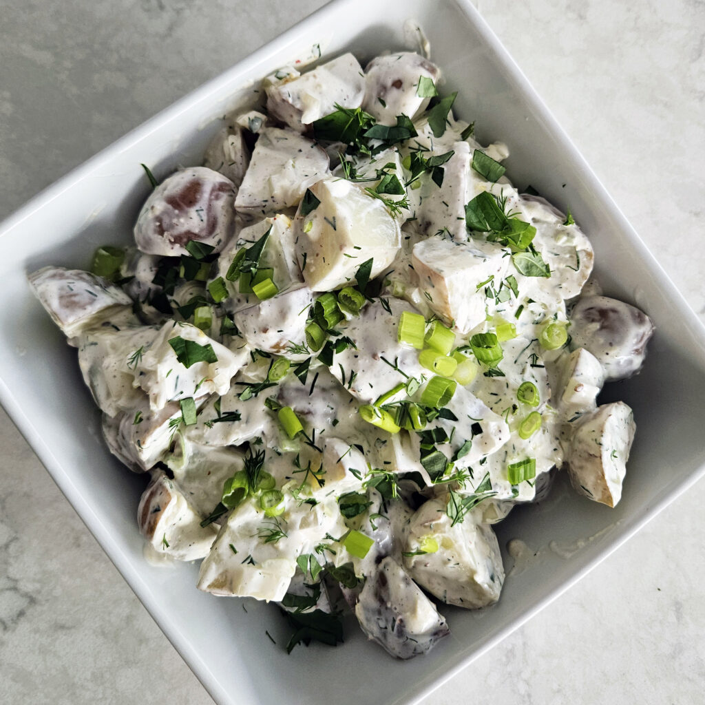 Creamy potato salad with fresh herbs and lemon zest served in a bowl.