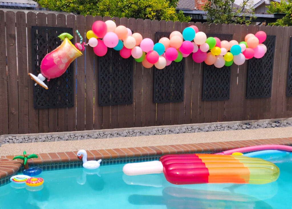 Balloon garland attached to a fence creating a festive luau pool party backdrop.