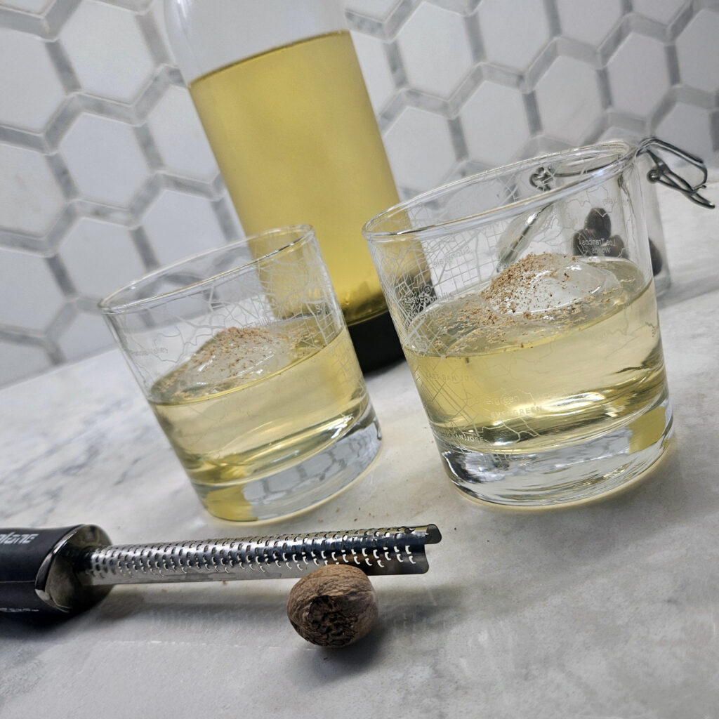 Crystal-clear milk punch served over ice in a rocks glass, showcasing its golden hue and polished, clarified finish.