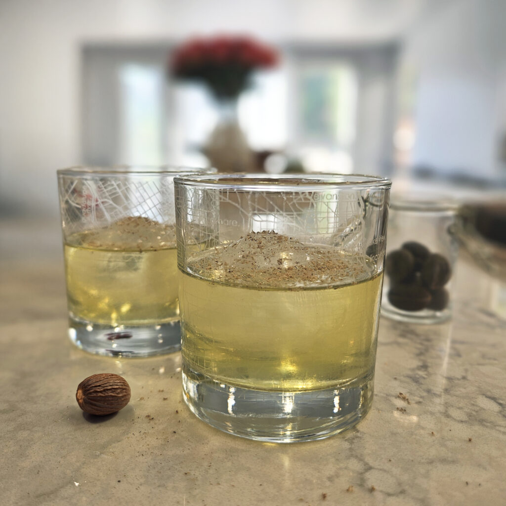 Crystal-clear milk punch served over ice in a rocks glass, showcasing its golden hue and polished, clarified finish.