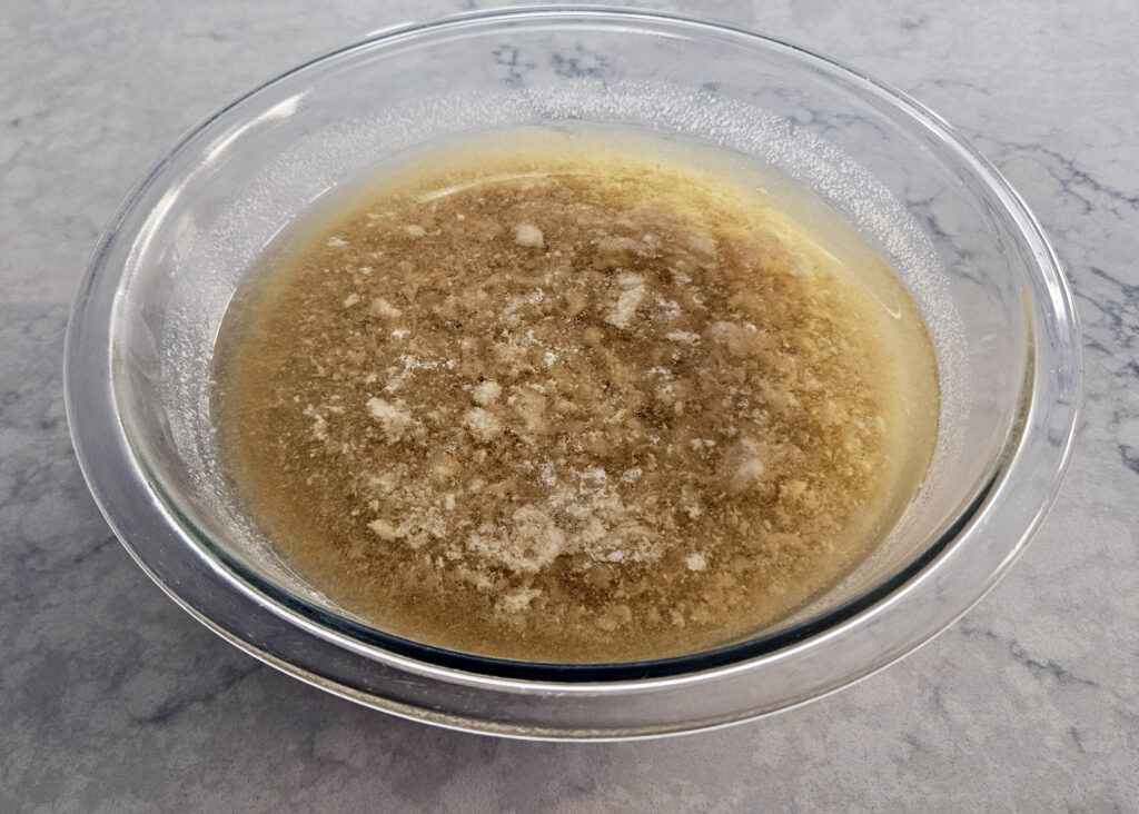 Milk punch mixture resting in the fridge as the milk curdles, forming a visible web of whey before straining.