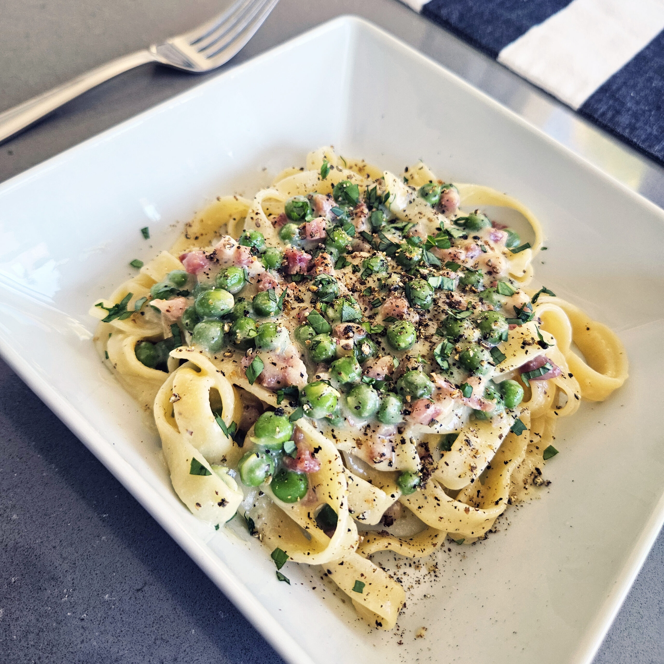 Fresh pasta carbonara with pancetta, peas, black pepper, and grated cheese, tossed in a glossy egg-based sauce.