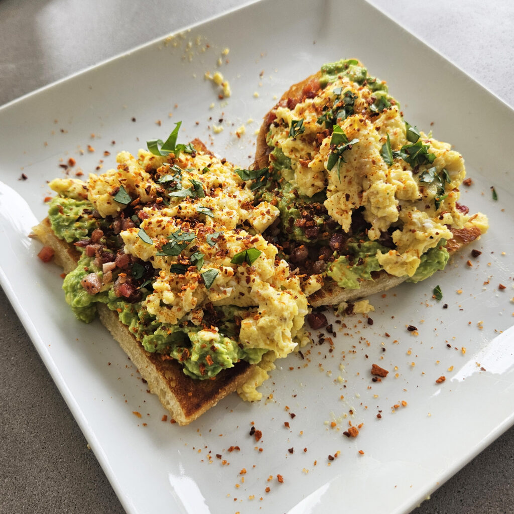 Whole grain avocado toast with sliced avocado, pancetta, and creamy soft scrambled eggs