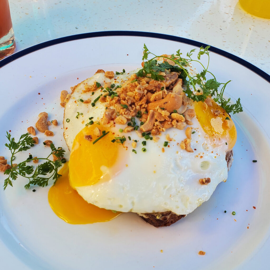 Rye avocado toast with chili crisp mash, pork belly, sunny-side-up egg, and crushed cashews
