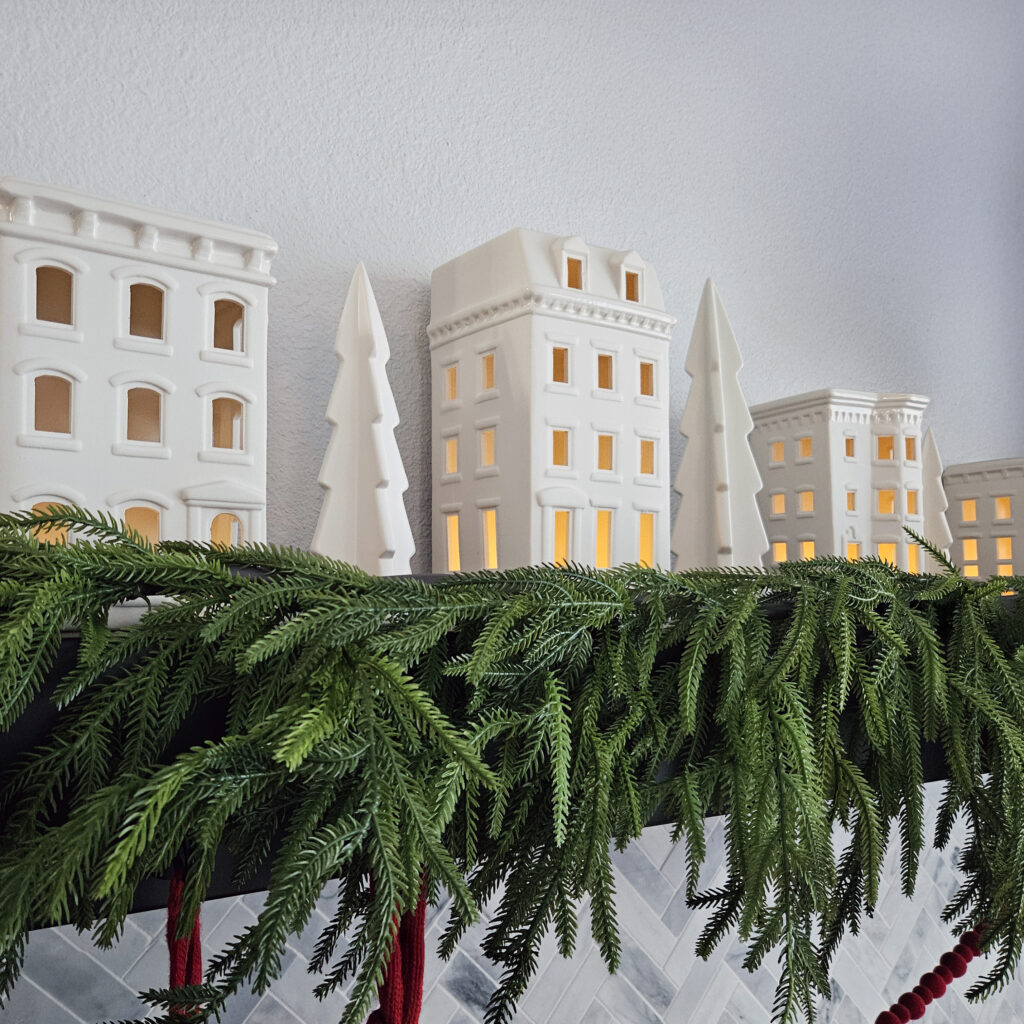 Christmas village pottery houses on black mantle with fir tree garland
