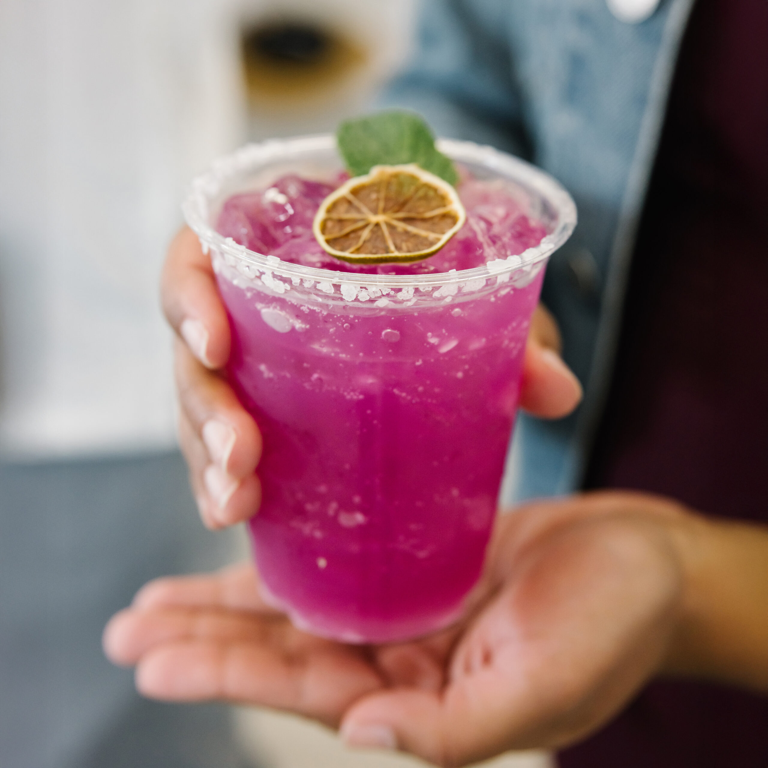 Prickly pear margarita with a salted rim, vibrant pink cocktail over ice, garnished with fresh lime on a light background.
