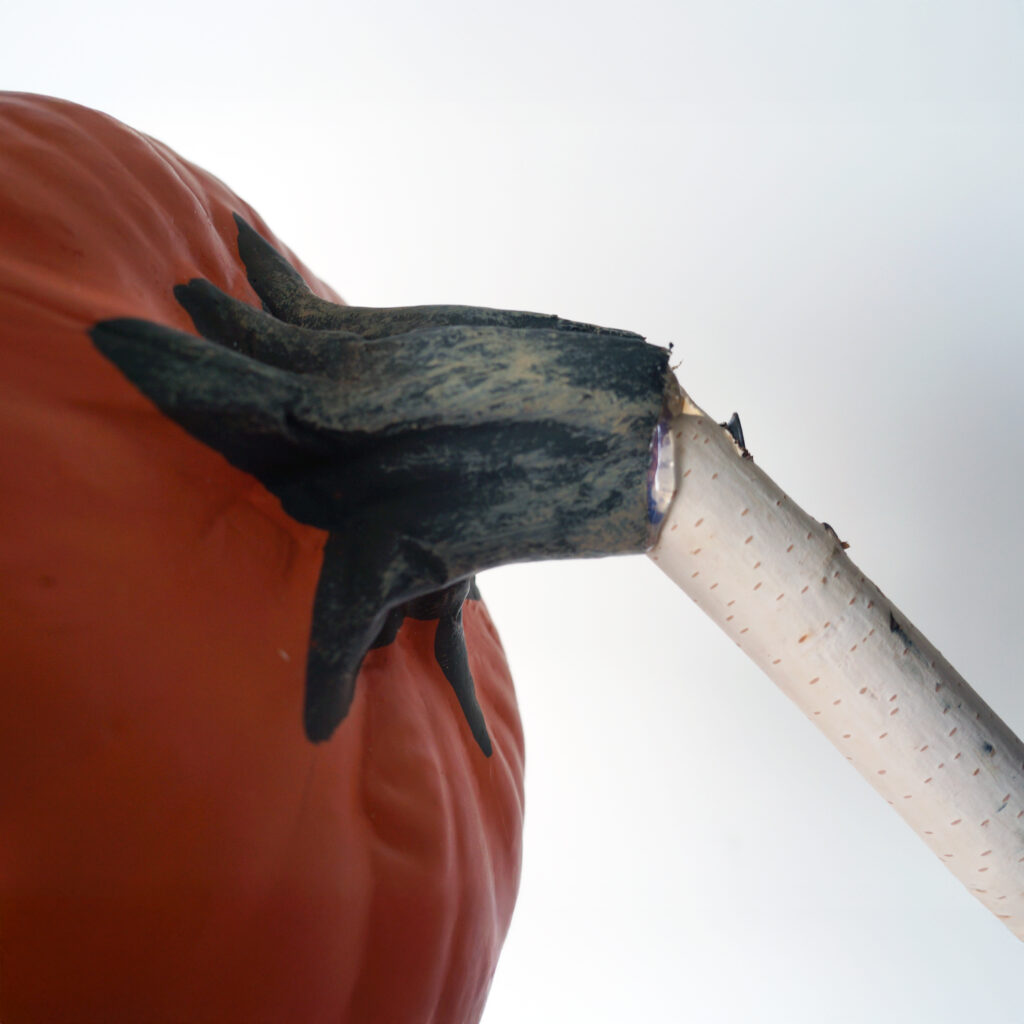 Close-up of a branch inserted into the bottom of a foam pumpkin, secured to form the stem of a giant fly trap.