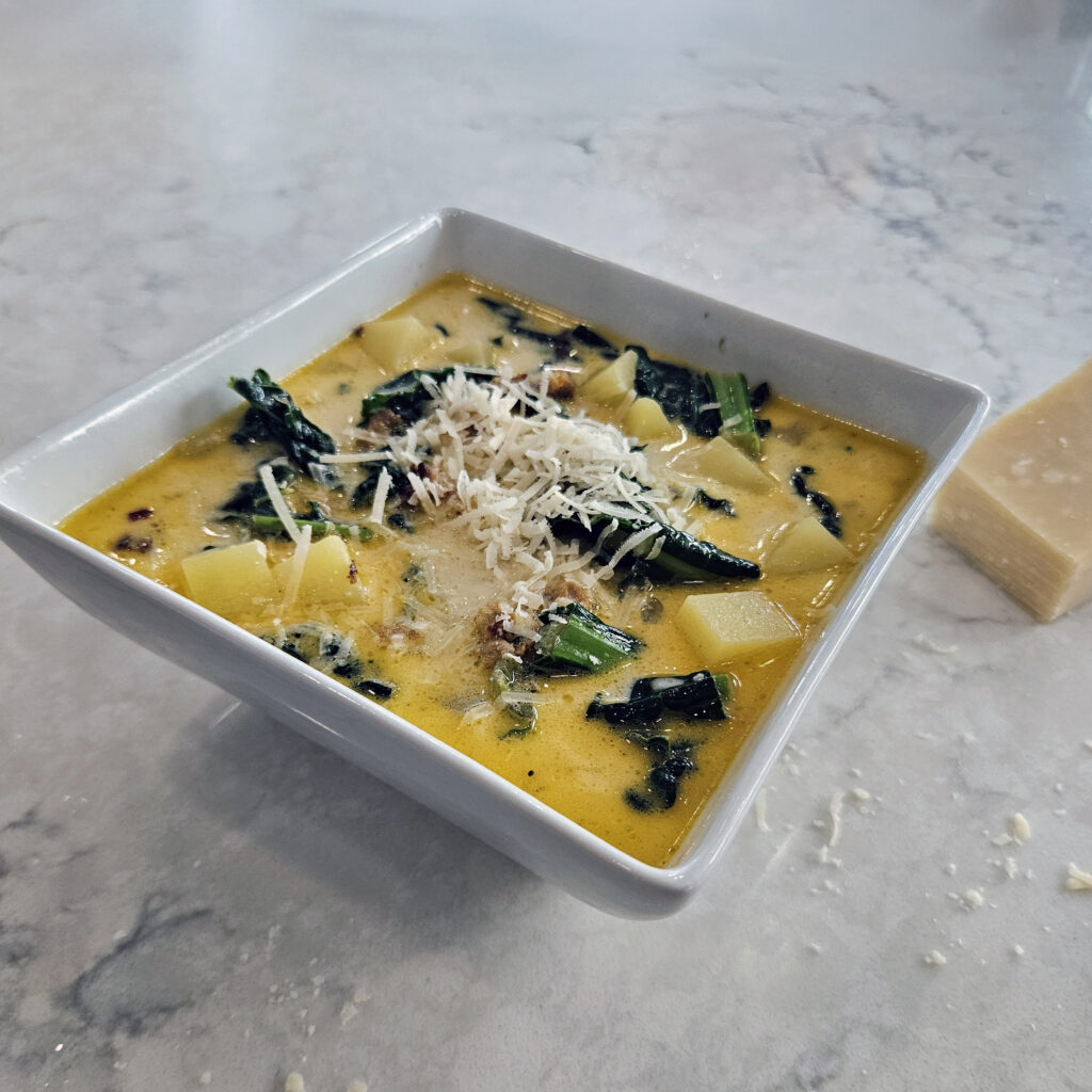 Creamy Italian sausage zuppa with potatoes and kale served in a bowl, rich broth with visible sausage and greens.
