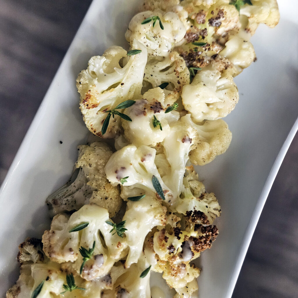 Roasted cauliflower florets with crispy caramelized edges served with creamy beer cheese sauce on a platter.
