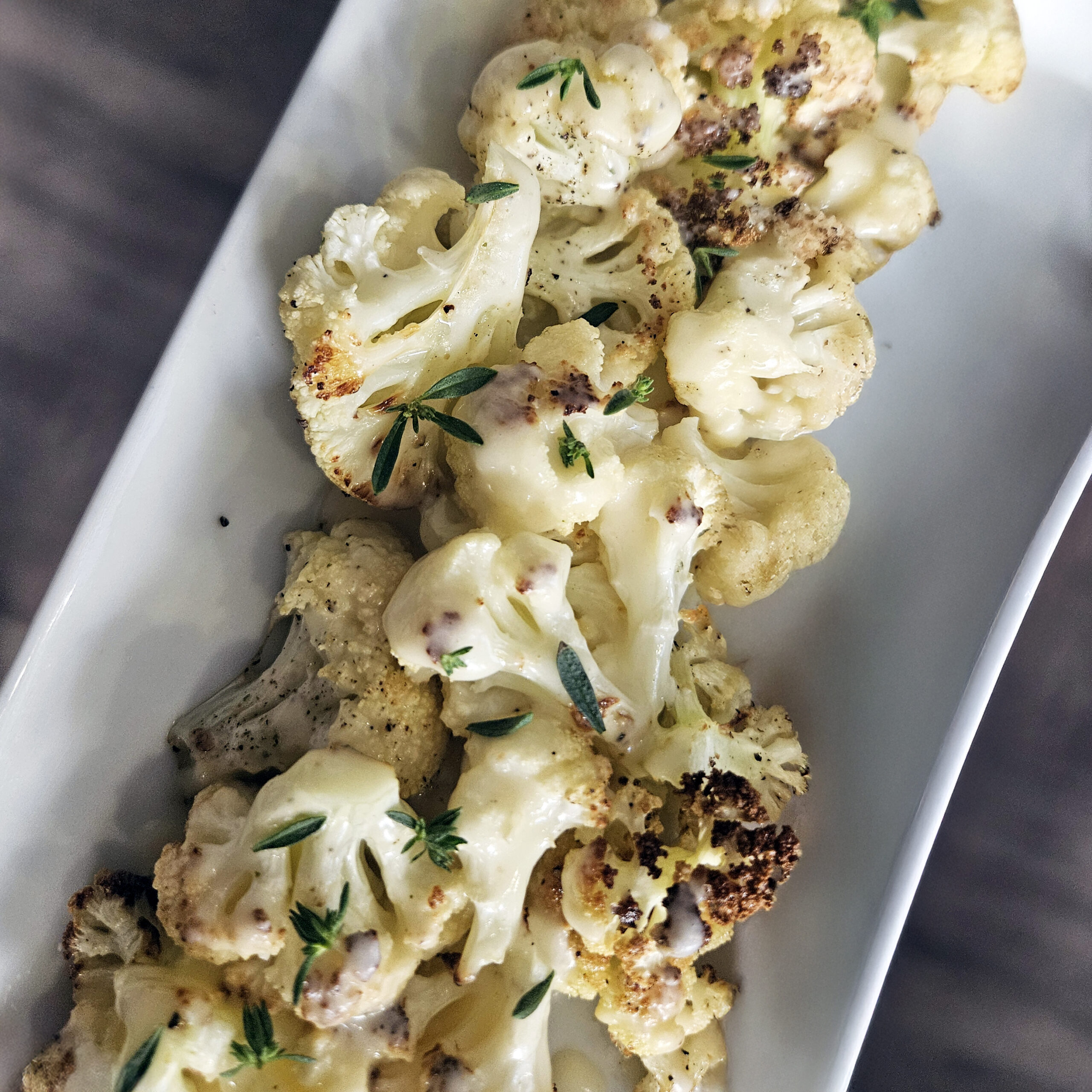 Roasted cauliflower florets with crispy caramelized edges served with creamy beer cheese sauce on a platter.