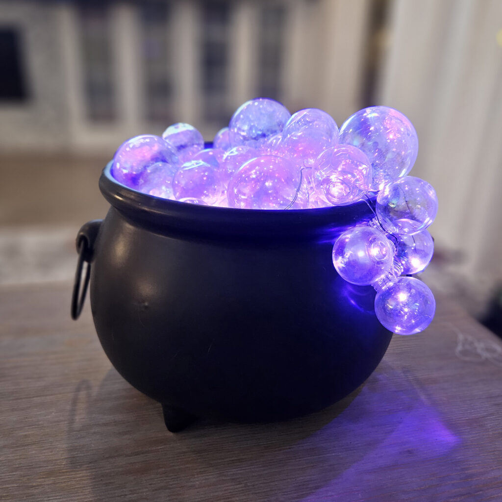 Fairy lights wrapped around ornament clusters with battery pack hidden inside the cauldron.